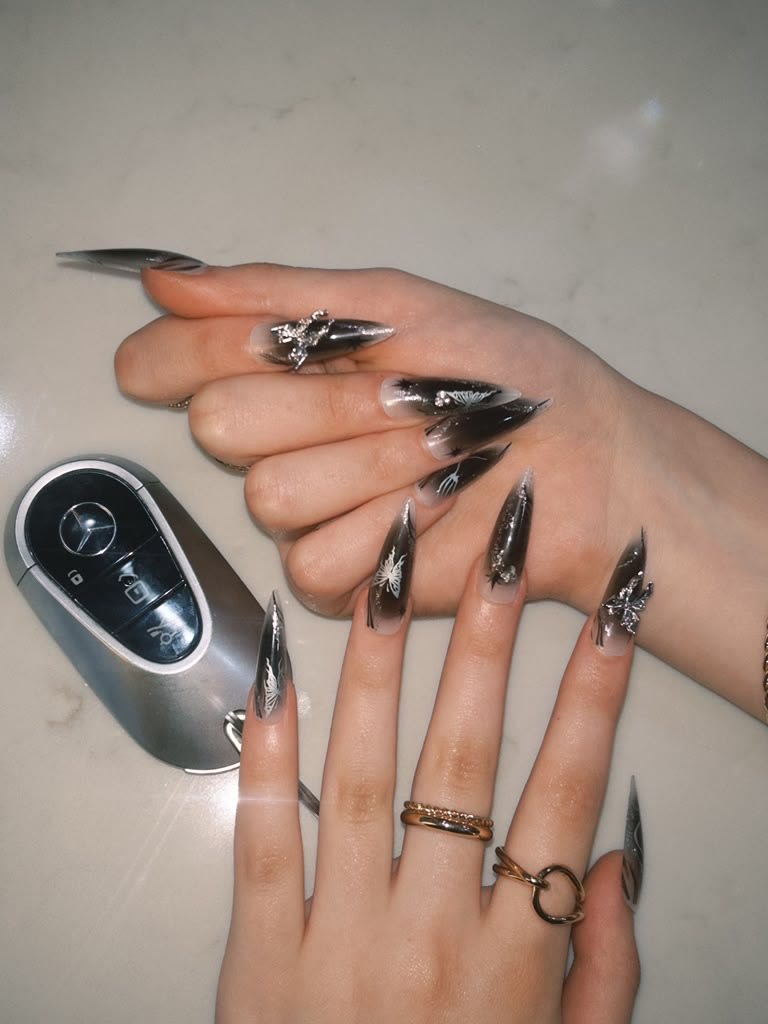 A hand with dark glossy Roselia nails resting beside a perfume bottle