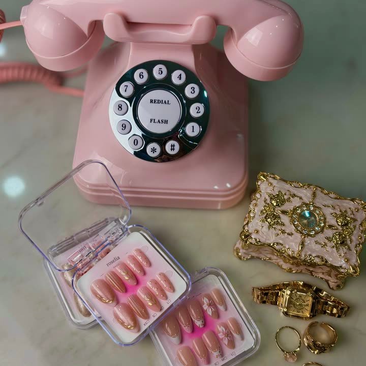 Gilded Tulip press-on nails, pink shimmer with gold tulip line art, beside a pink rotary telephone and vintage jewellery